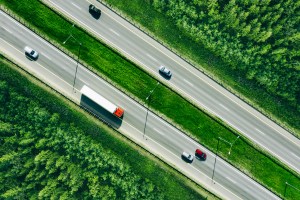 Aerial drone view of highway asphalt road with cars and trucks driving through green summer woods. Cargo delivery logistic concept