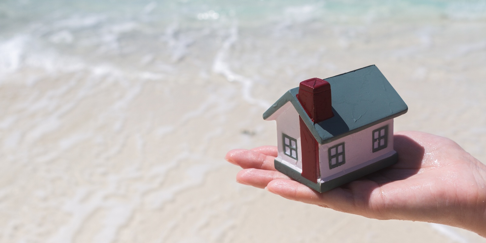 A toy house on an open palm on a background of water depicting the benefits of flood insurance