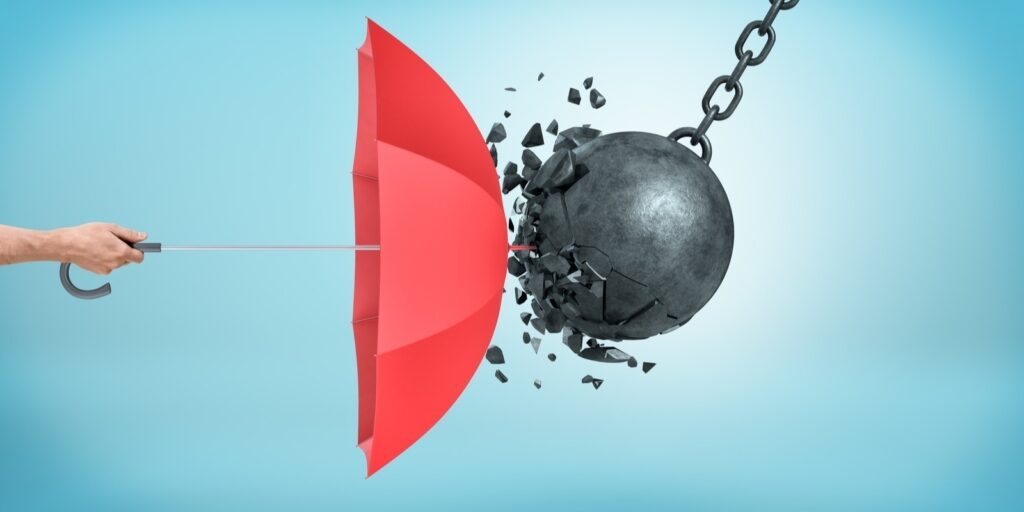 male hand holding an open red umbrella which protects from a collision with a broken wrecking ball