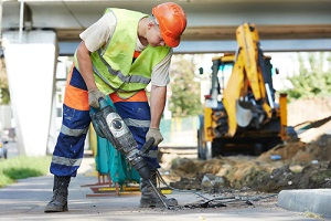 worker with pneumatic hammer drill equipment breaking asphalt at road needing construction insurance