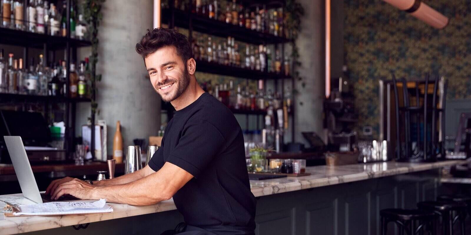 owner of restaurant bar sitting at counter working on laptop
