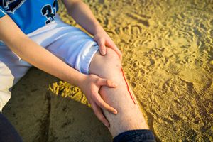 Sports person wearing blue t-shirt and white shorts holding his bleeding left knee