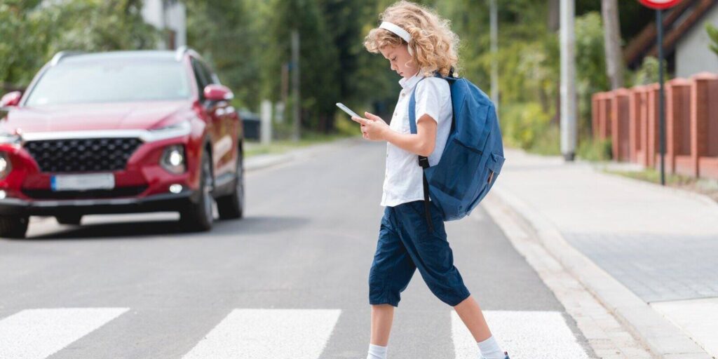 small kid crossing road while looking on the phone