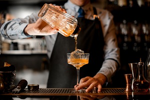 barman gently pours finished cocktail from glass shaker into glass.