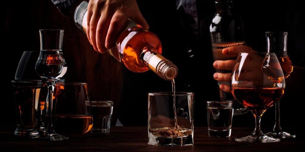 bartender pours the dark golden rum in glass on the old bar counter