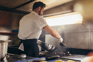 cook making some food in a food truck parked under a tree