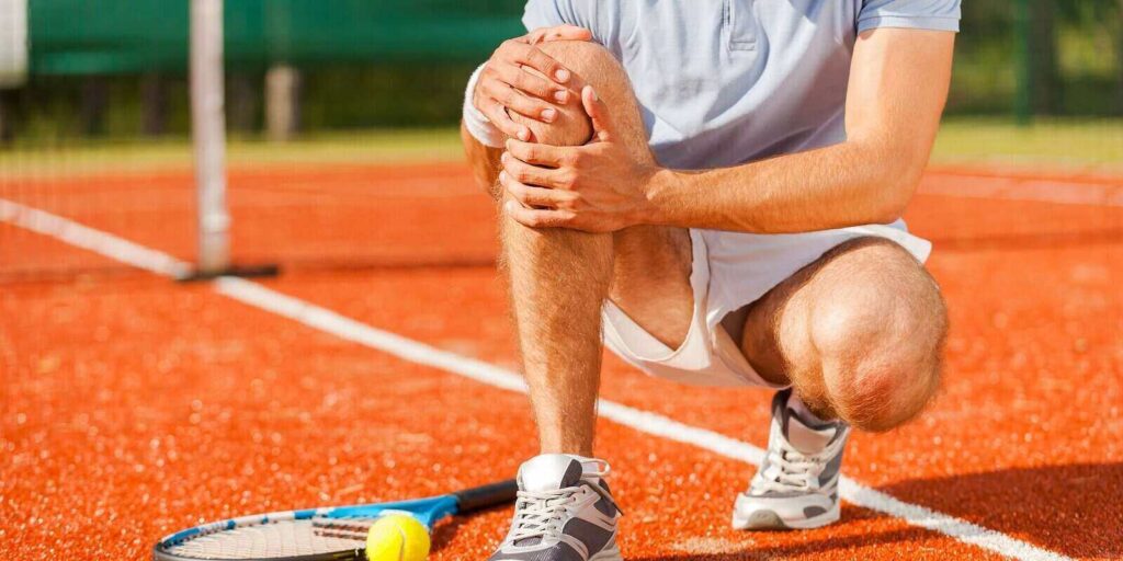 tennis player touching his knee while sitting on the tennis court