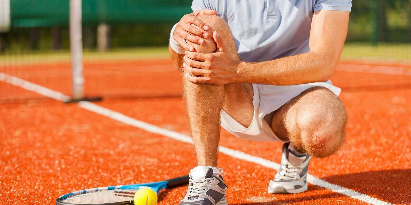tennis player touching his knee while sitting on the tennis court