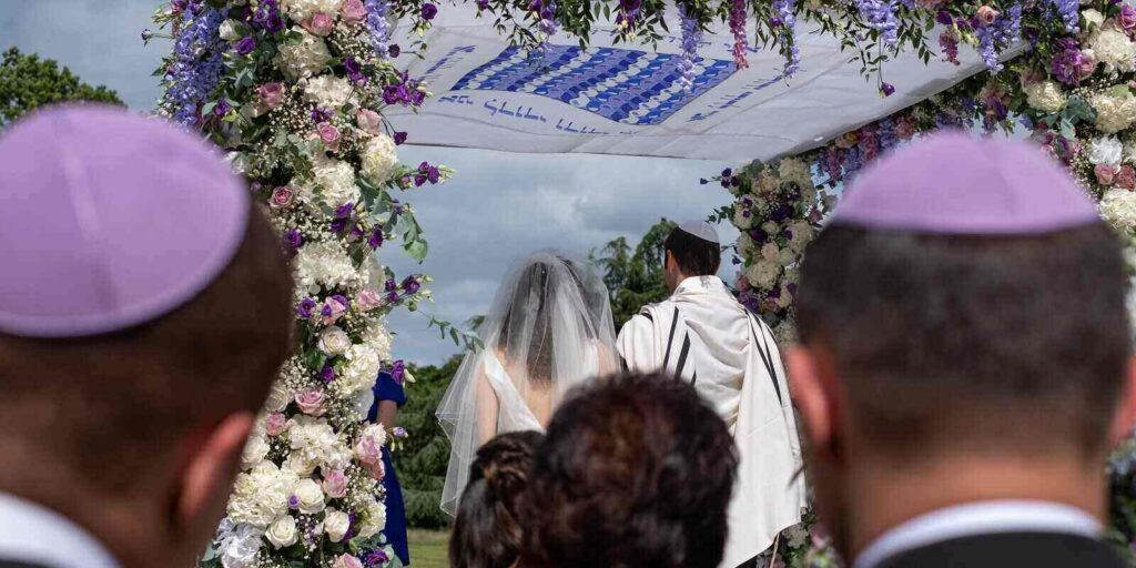 couple at a marriage ceremony under a floral chuppa wedding canopy
