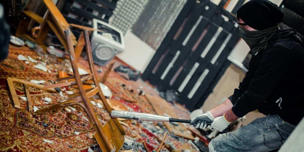 man in the rage room smashing chair and old computer with a baseball bat