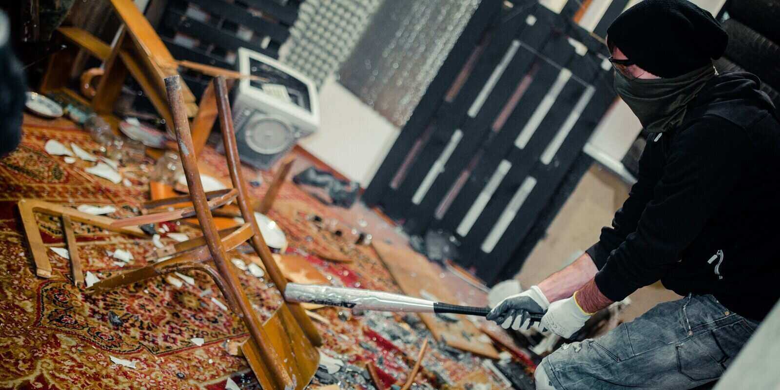 man in the rage room smashing chair and old computer with a baseball bat