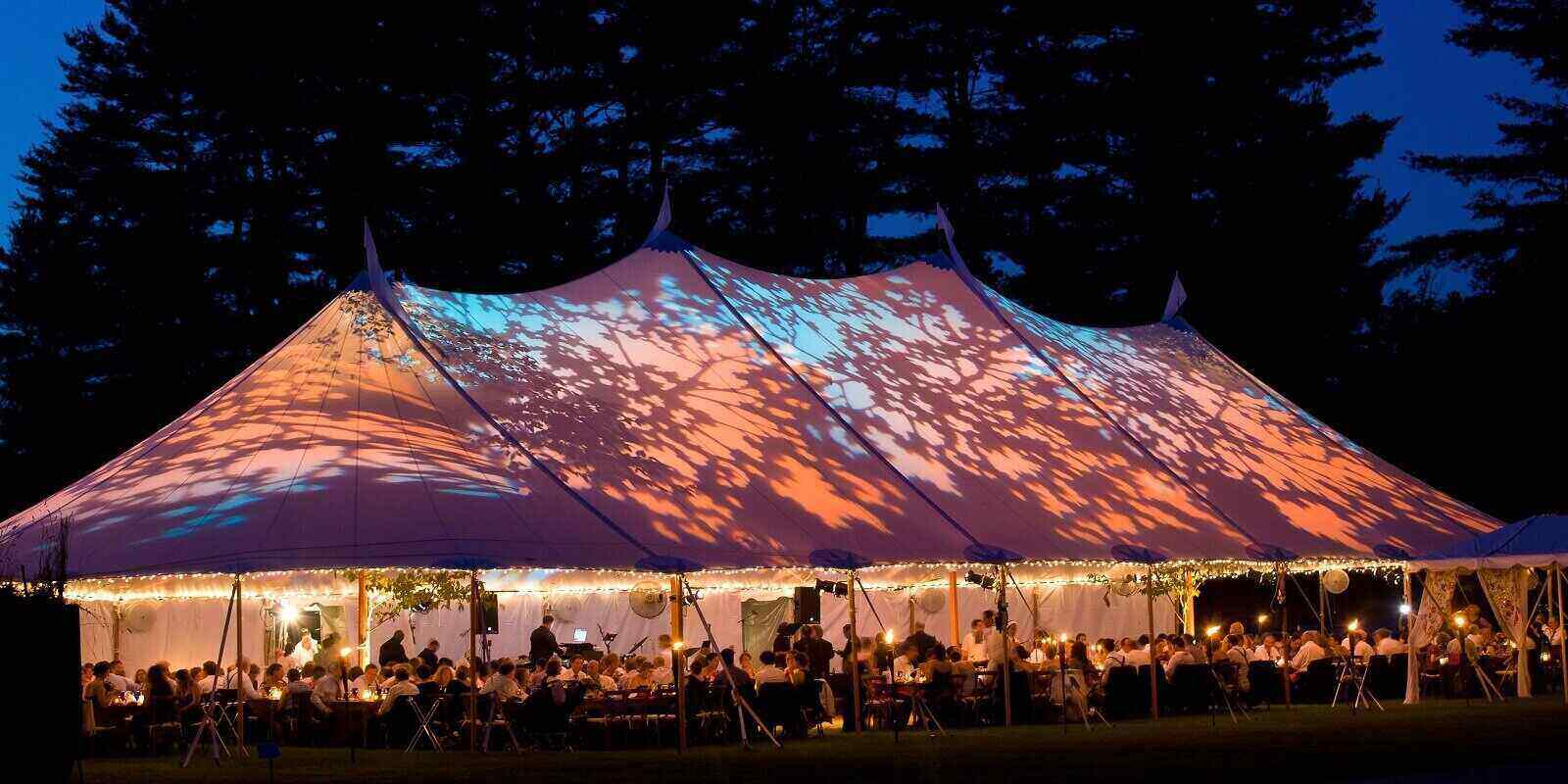 special event tent lit up from the inside with dark blue night time sky and trees