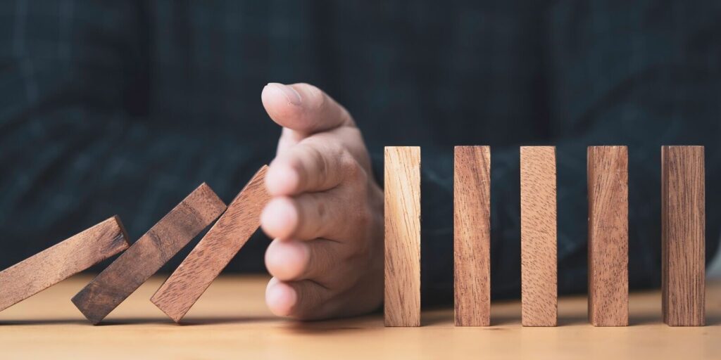 businessman uses his hand to stop a falling wooden block to a standing wooden block domino