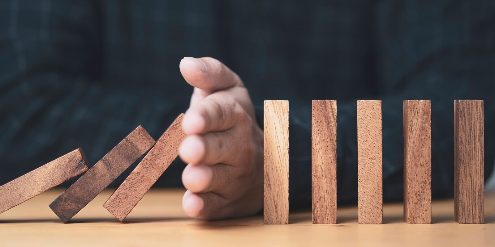 businessman uses his hand to stop a falling wooden block to a standing wooden block domino