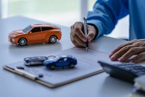 man signing a document with car keys and dummies on table