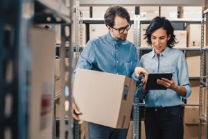 female inventory manager shows digital tablet information to a worker holding cardboard box
