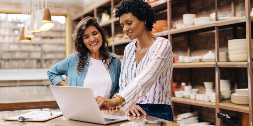successful female ceramists using a laptop together in their store