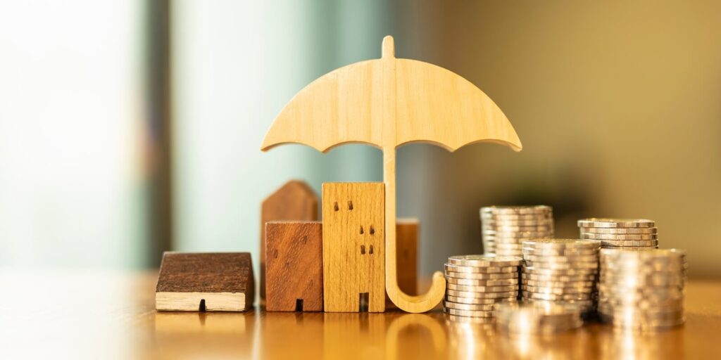 umbrella with house and coins on wooden table concept of the system of insurance savings and the cost of health insurance