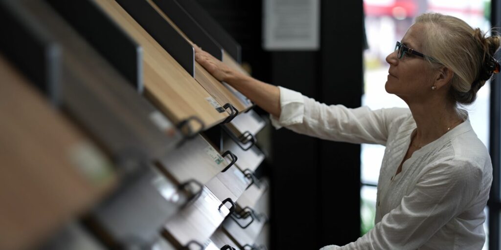 mature woman running hand across solid or engineered wood plank samples in a floor or hardware store for a home remodeling renovation project