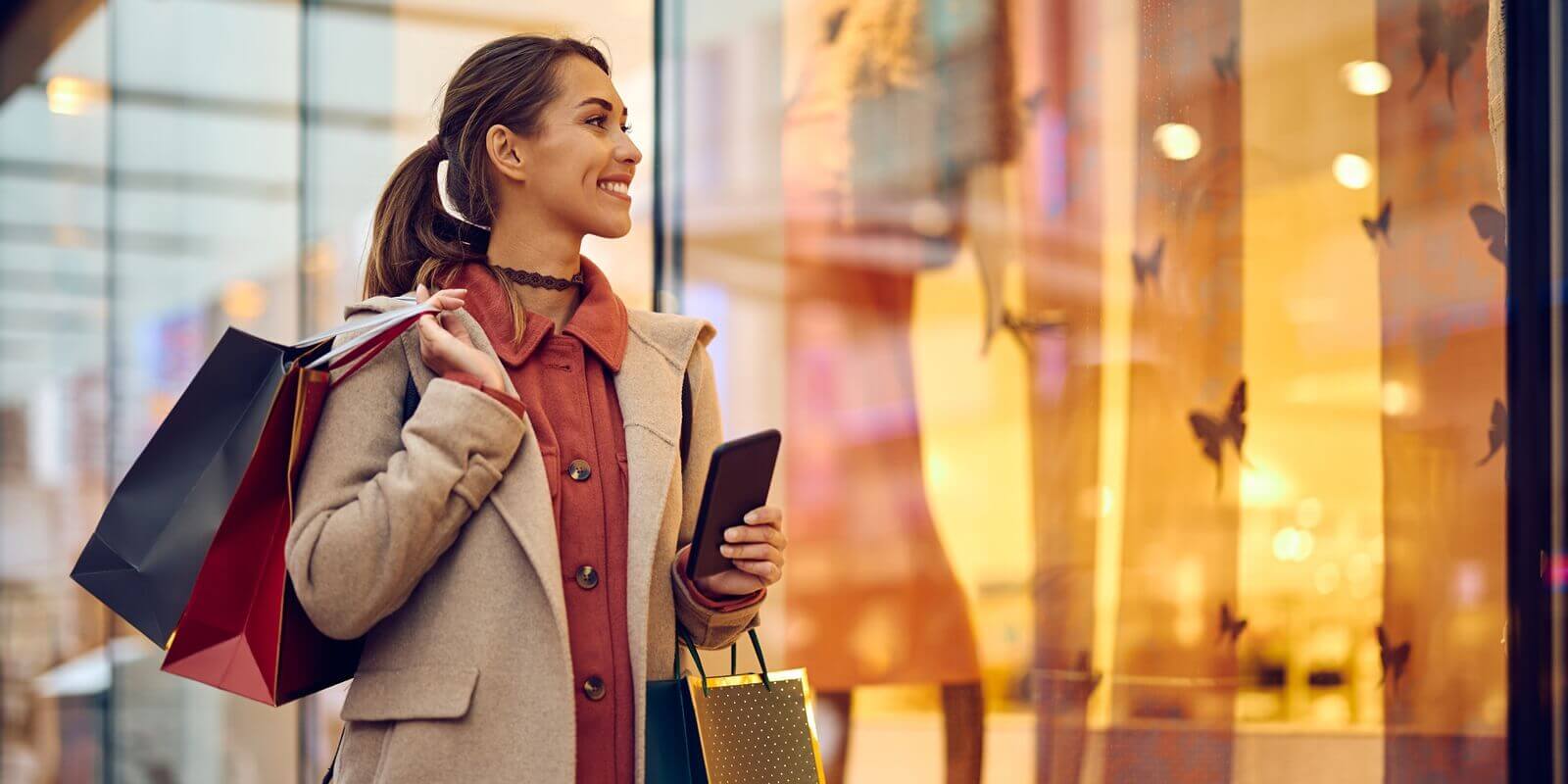 happy woman with shopping bags looking at store windows while walking through city