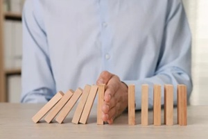 man stopping wooden blocks from falling at table, closeup