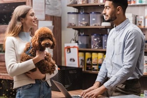 side view of smiling woman holding poodle near arabian seller in pet shop