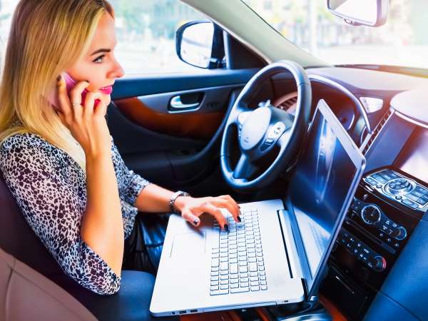 Woman using a laptop and smartphone in her car