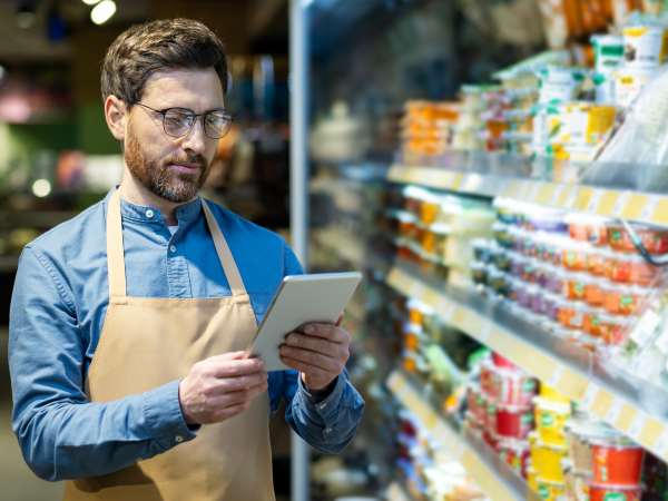 Grocery store manager using digital tablet for product inventory and stock analysis in supermarket aisle with dairy products