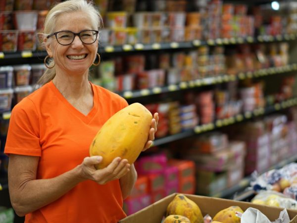 Closeup portrait of smiling happy pretty mature woman selecting a papaya fruit in a grocery store.