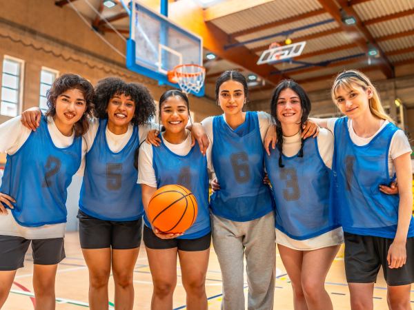 Diverse group of female basketball players hugging and holding ball, showcasing team unity and athletic spirit