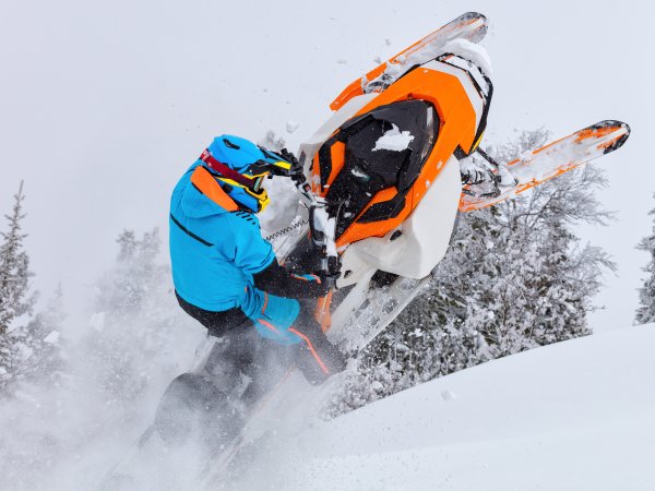 A man is riding snowmobile in mountains. jump on a snow bike. pilot on a sports snowmobile in a mountain forest. The concept of skidooking. rider in a bright suit on a colorful snowy moto