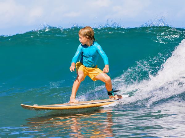 Happy surf boy - young surfer learn to ride on surfboard with fun on sea waves. Active family lifestyle, kids outdoor water sport lessons, swimming activity in surfing camp. Summer vacation with child