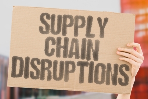 Hand Holding A Board with Supply Chain Disruptions Text