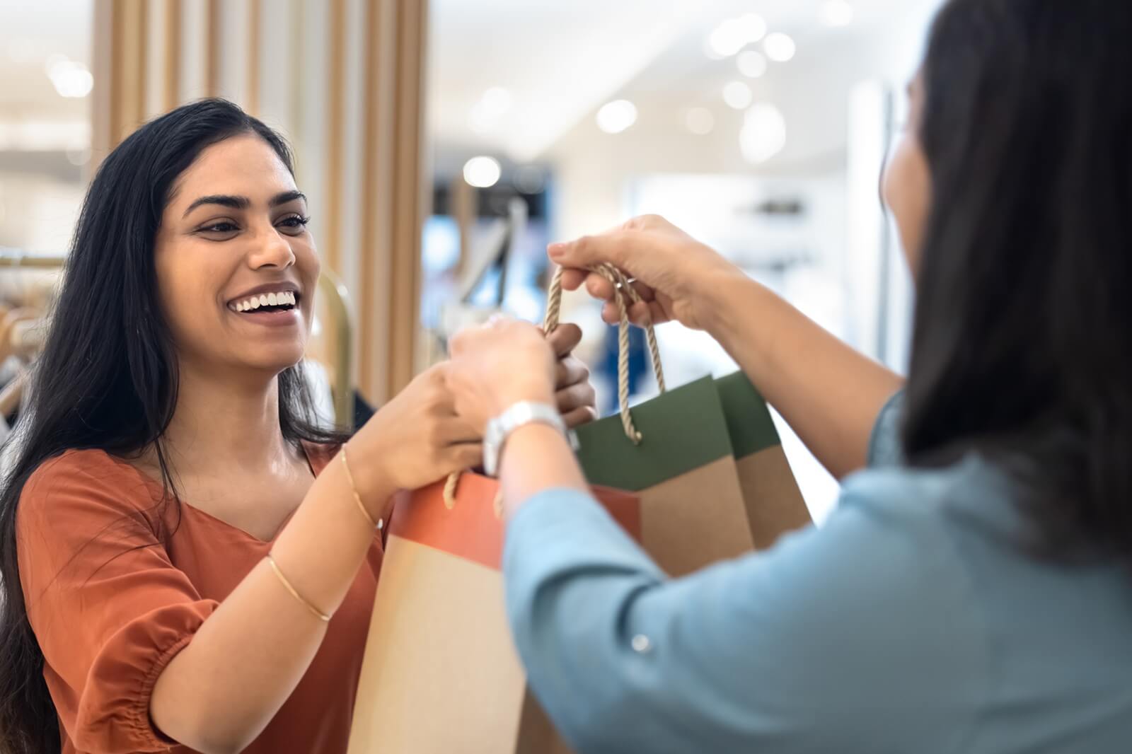 cheerful indian customer taking shopping bags with clothes from associate