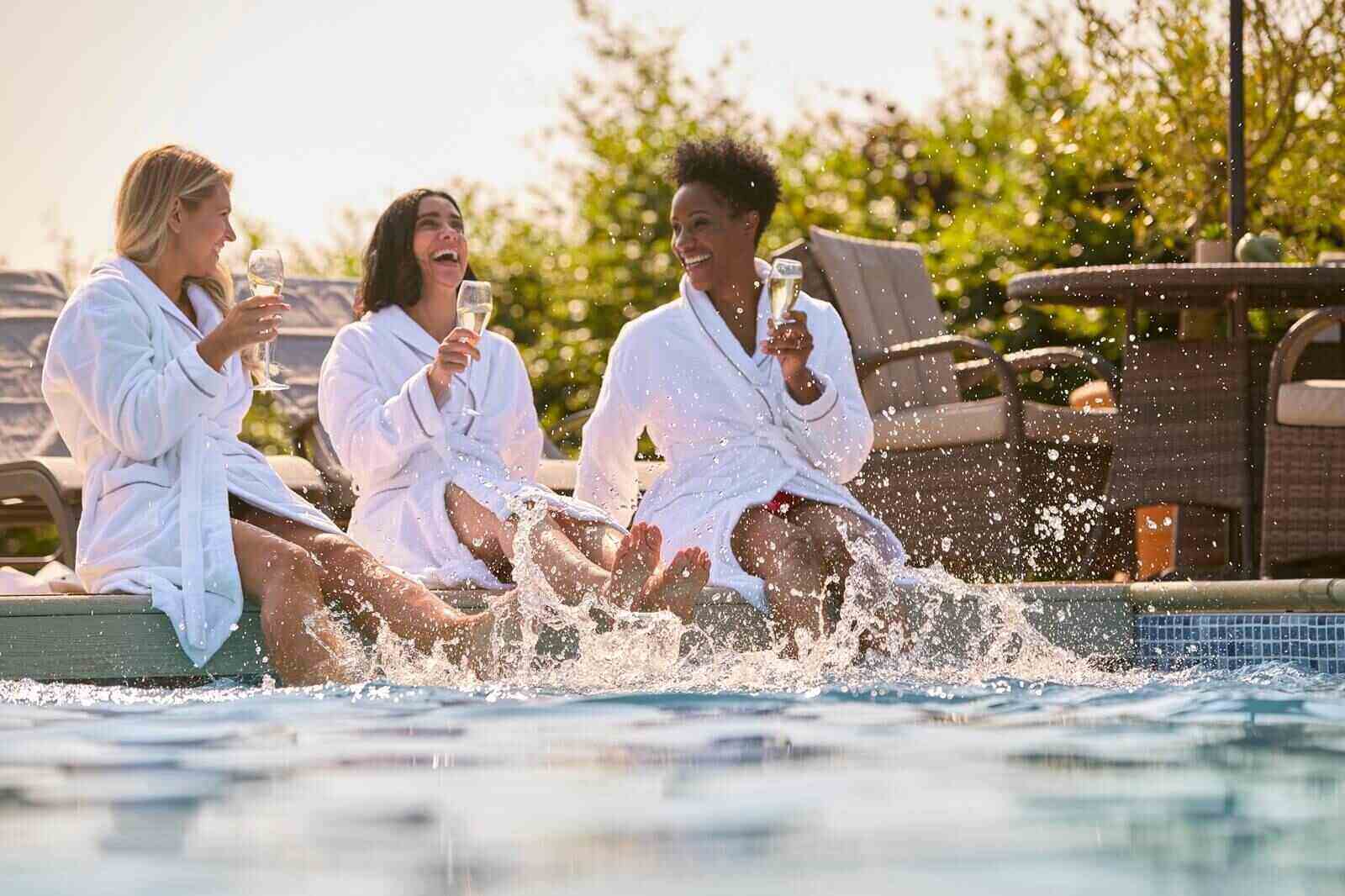 female friends wearing robes sitting with feet in pool