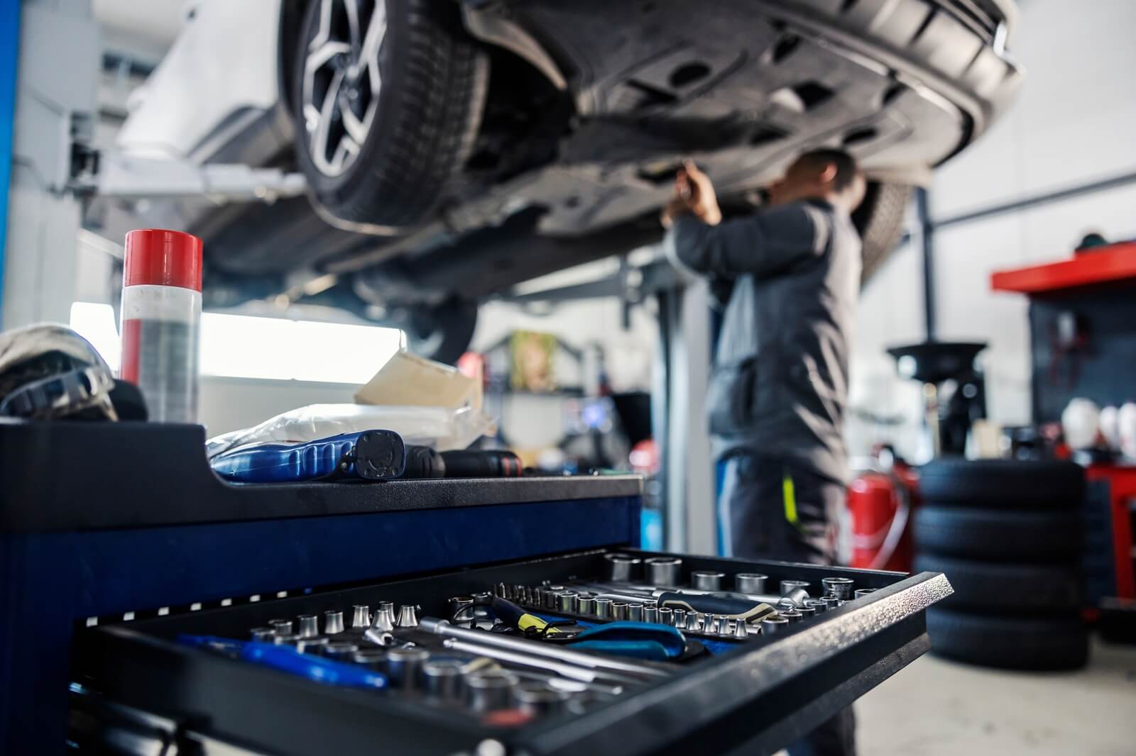 focus on a tools in toolbox at mechanic's shop with mechanic repairing the car in blurry background