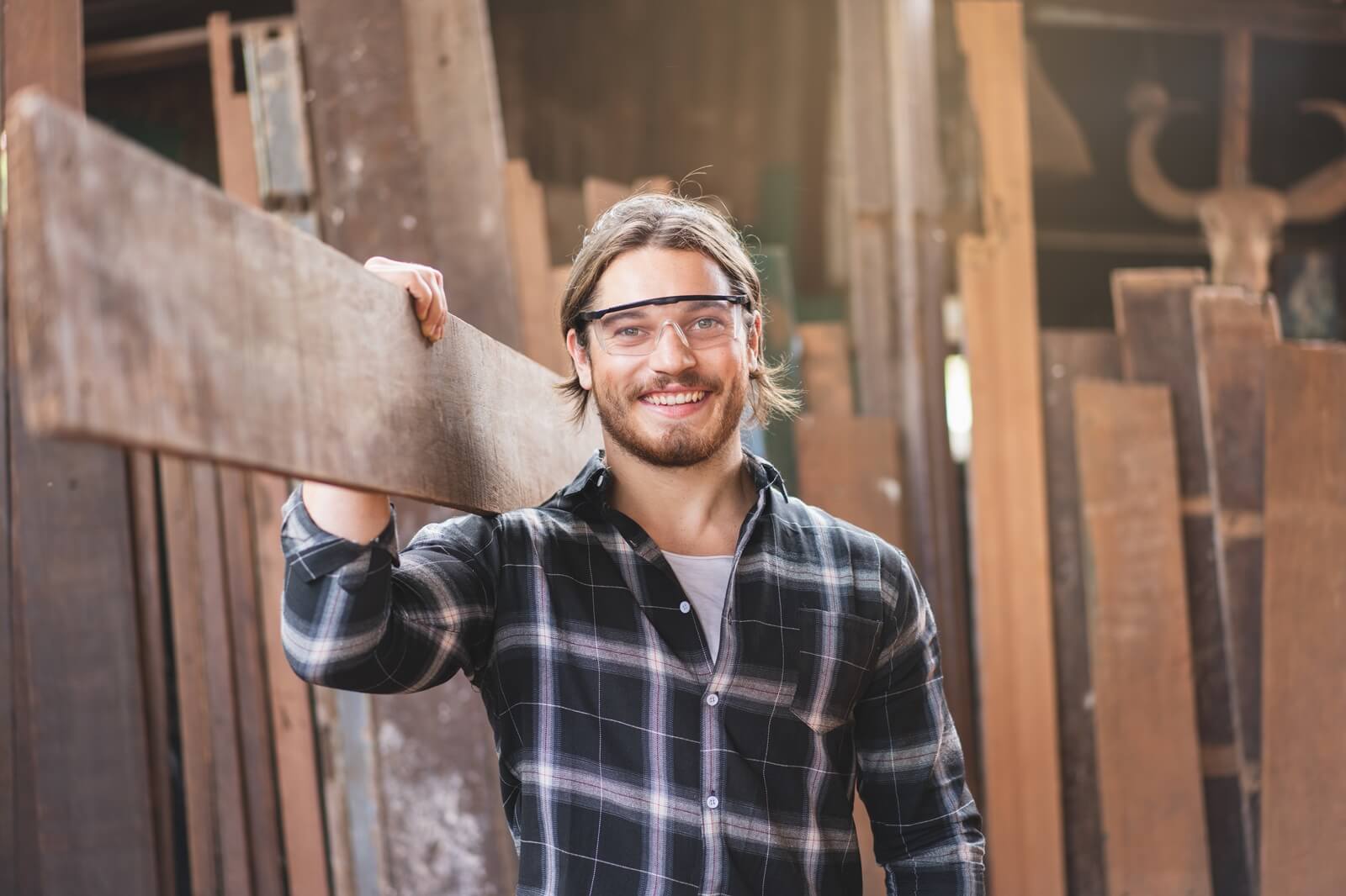 male carpenter worker smiling while hold wooden plank at the carpentry workshop