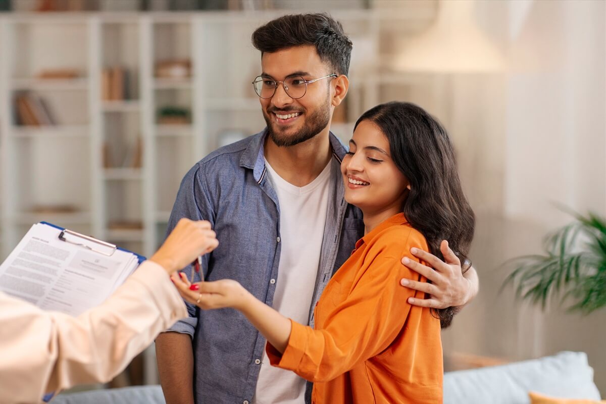real estate agent giving keys to young indian buyers