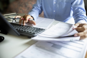 Retail Shop Owner Doing Inventory Valuation with Calculator and Documents