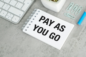 Pay-As-You-Go Text Written on A White Notebook Near Laptop