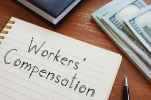 Workers Compensation Written on Notebook Near Stack of Dollars