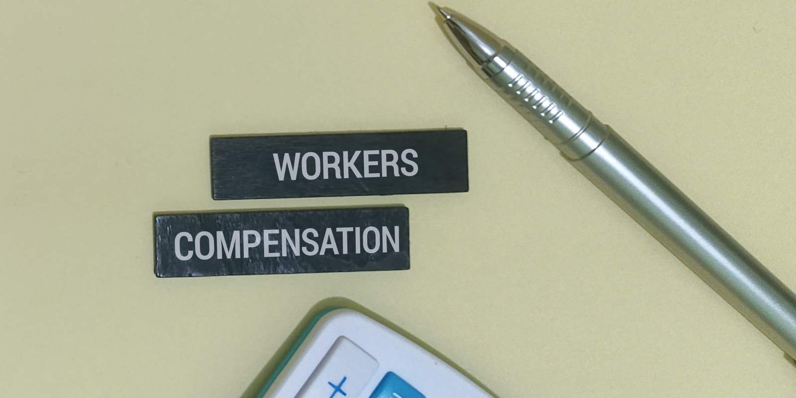 Blocks with Workers Compensation Text Near Pen and Calculator