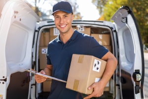 Delivery Man Standing Carrying A Box and Clipboard in Front of His Van
