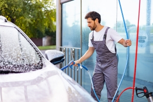 Man Using a High-Pressure Washer to Clean a Car Covered in Soap at Washing Center