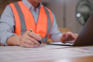 Contractor Wearing Safety Vest Reviewing Insurance Documents While Using Laptop at Work Desk