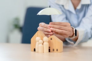 Hands Protecting a Wooden House and Family Figures Representing Homeowners Insurance Concept