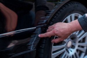Man Inspecting Scratch on Black Car for Repair
