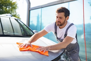 Smiling Car Wash Worker Carefully Cleaning Hood of a Car with an Orange Microfiber Cloth